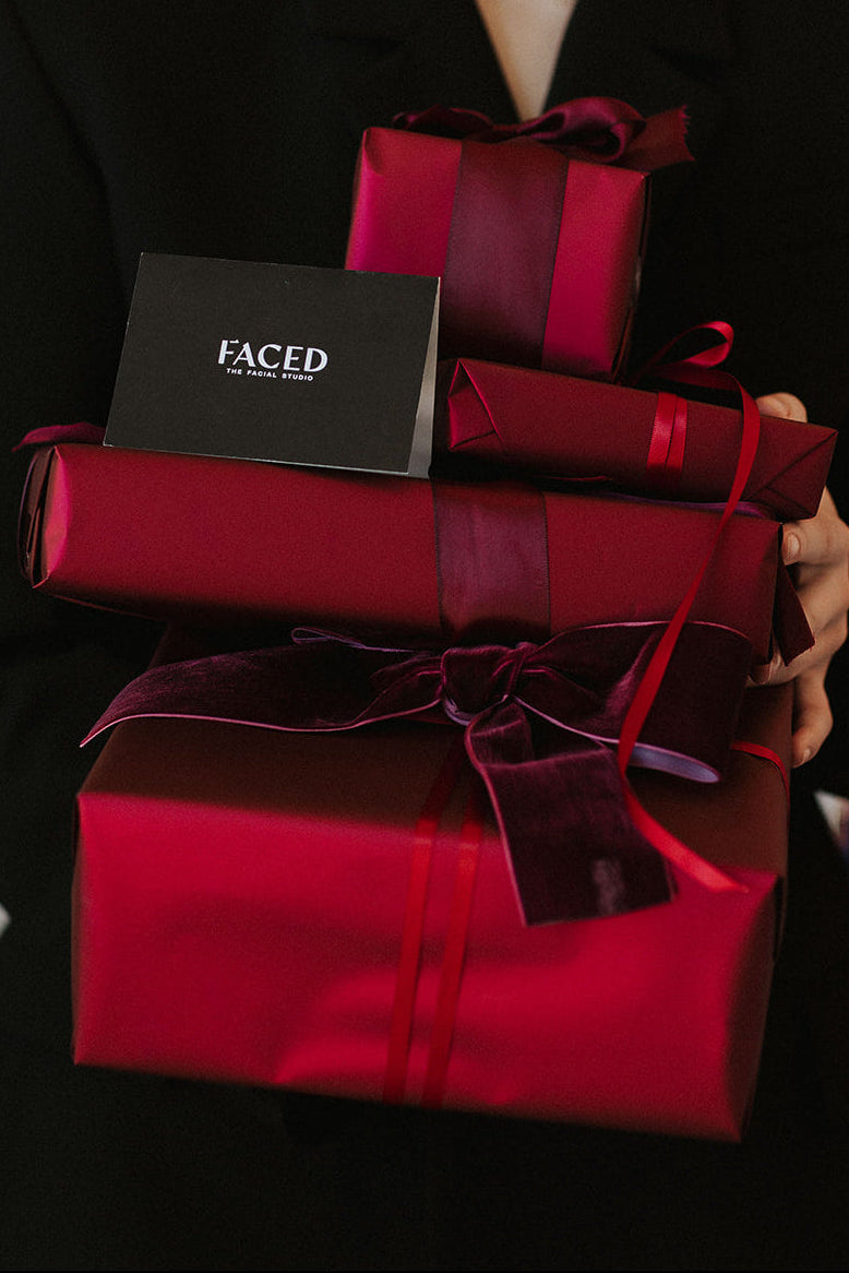 Person holding three red gift boxes with ribbons, one featuring a 'Faced' box.